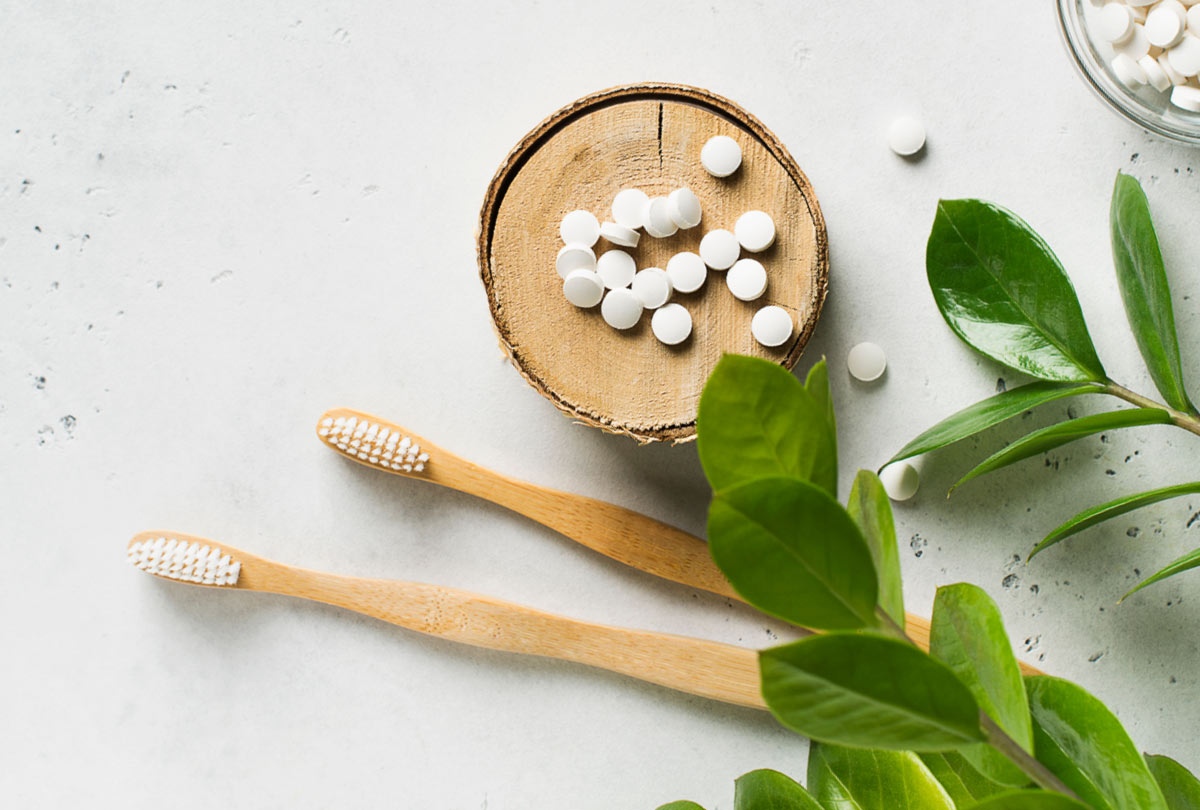 Two toothbrushes next to toothpaste tablets with mint overlaying. Text which reads "Should I trade my toothpaste tube for toothpaste tablets?"