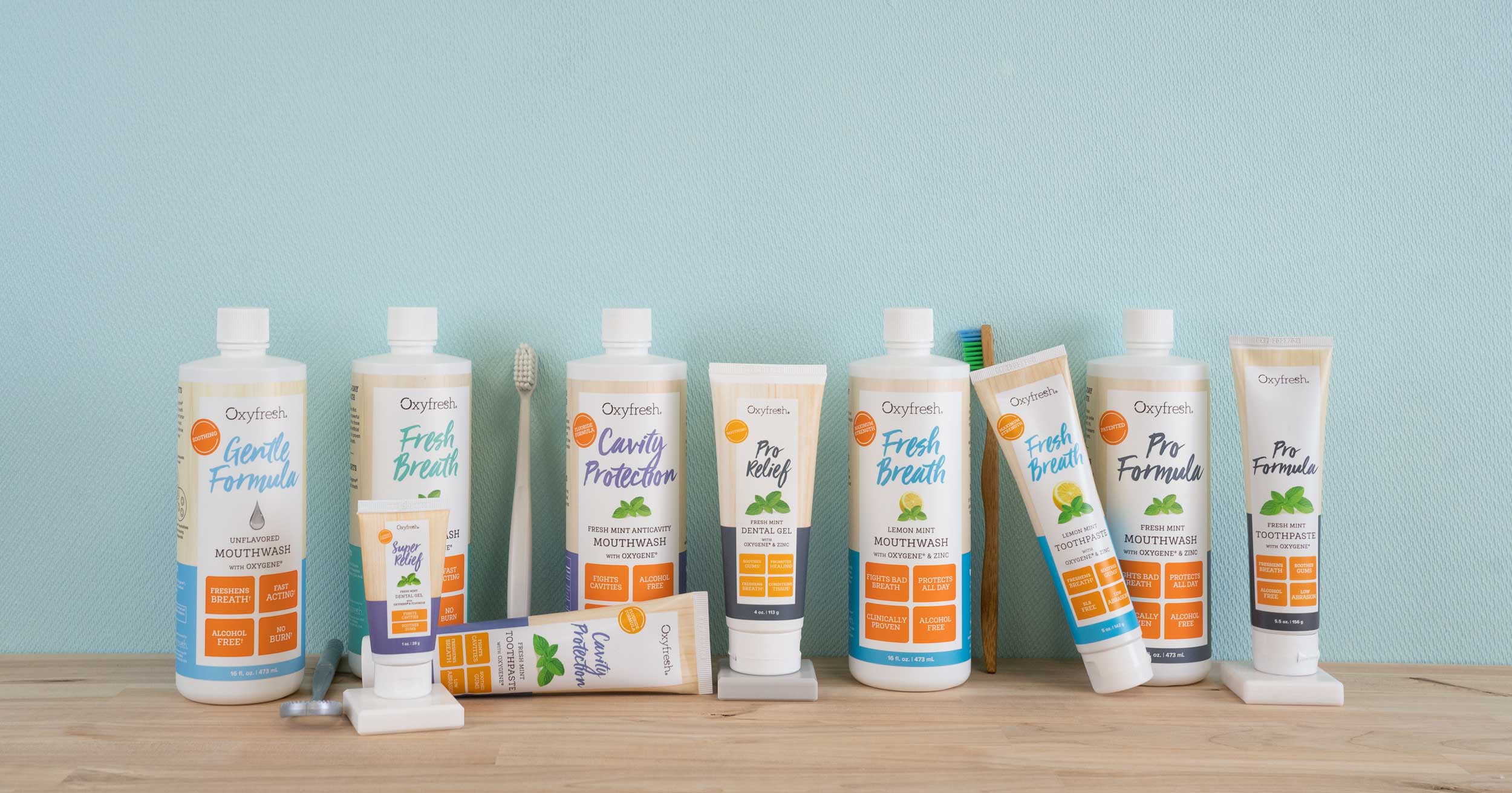 oxyfresh human dental care line bottles of mouthwash toothpaste and dental gels in a line in front of a blue textured background