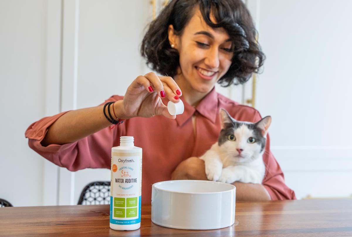 smiling-woman-holding-cat-while-pouring-oxyfresh-cat-water-additive-from-walmart-helps-fight-plaque-and-tartar