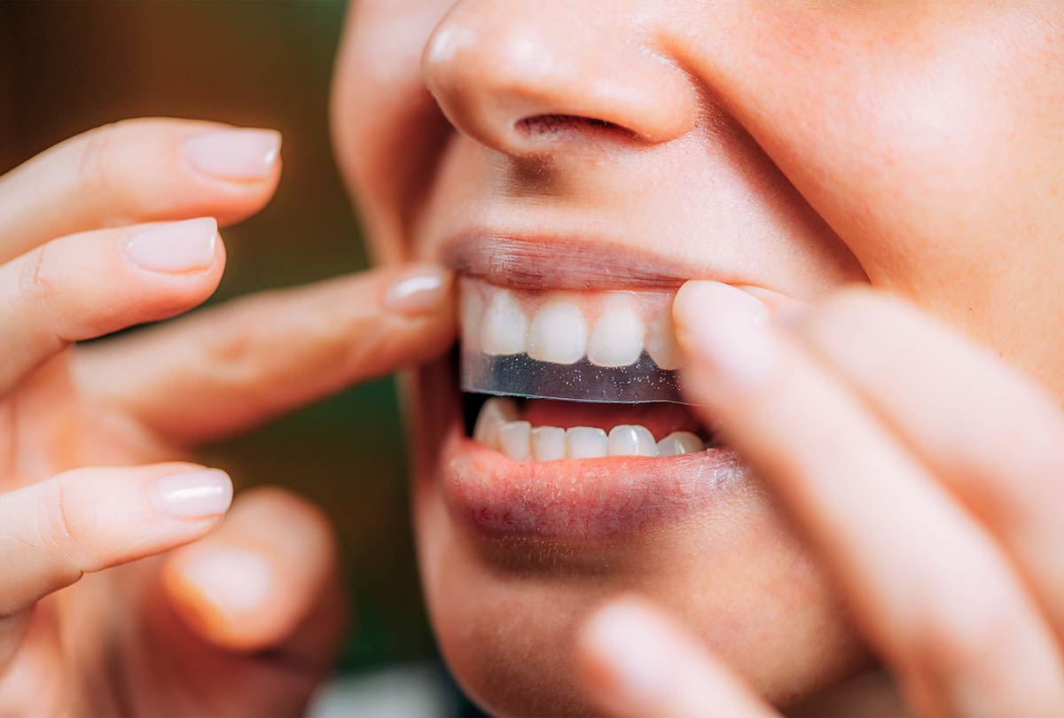 oxyfresh dental care image of woman placing whitening strip on her top row of teeth for the blog post titled Ouch! My Teeth Hurt After Whitening_3 Mus
